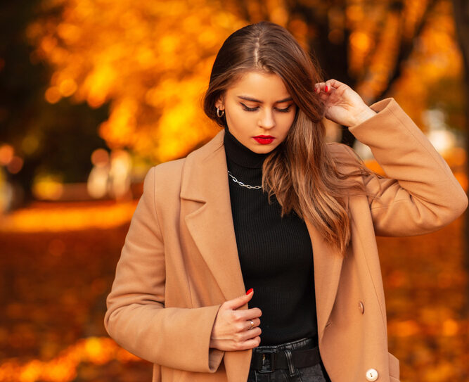 Donna con cappotto beige e capelli lisci dopo trattamento di nanoplastia Rivoli, passeggia tra foglie autunnali dorate.