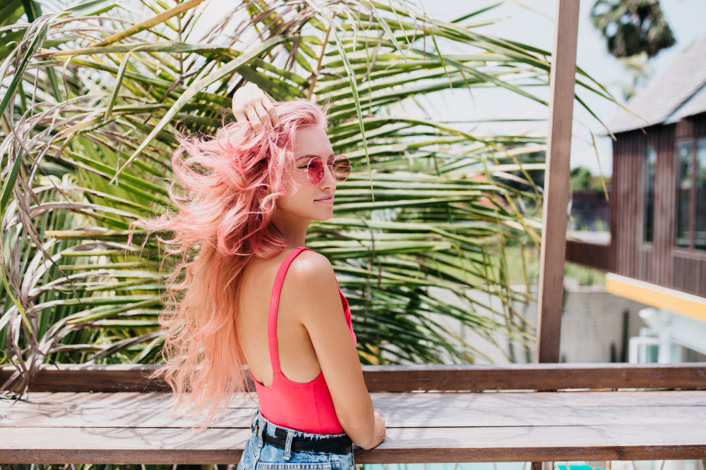 Ragazza con capelli rosa mossa dal vento che mostra gli effetti del sole sui capelli in estate.